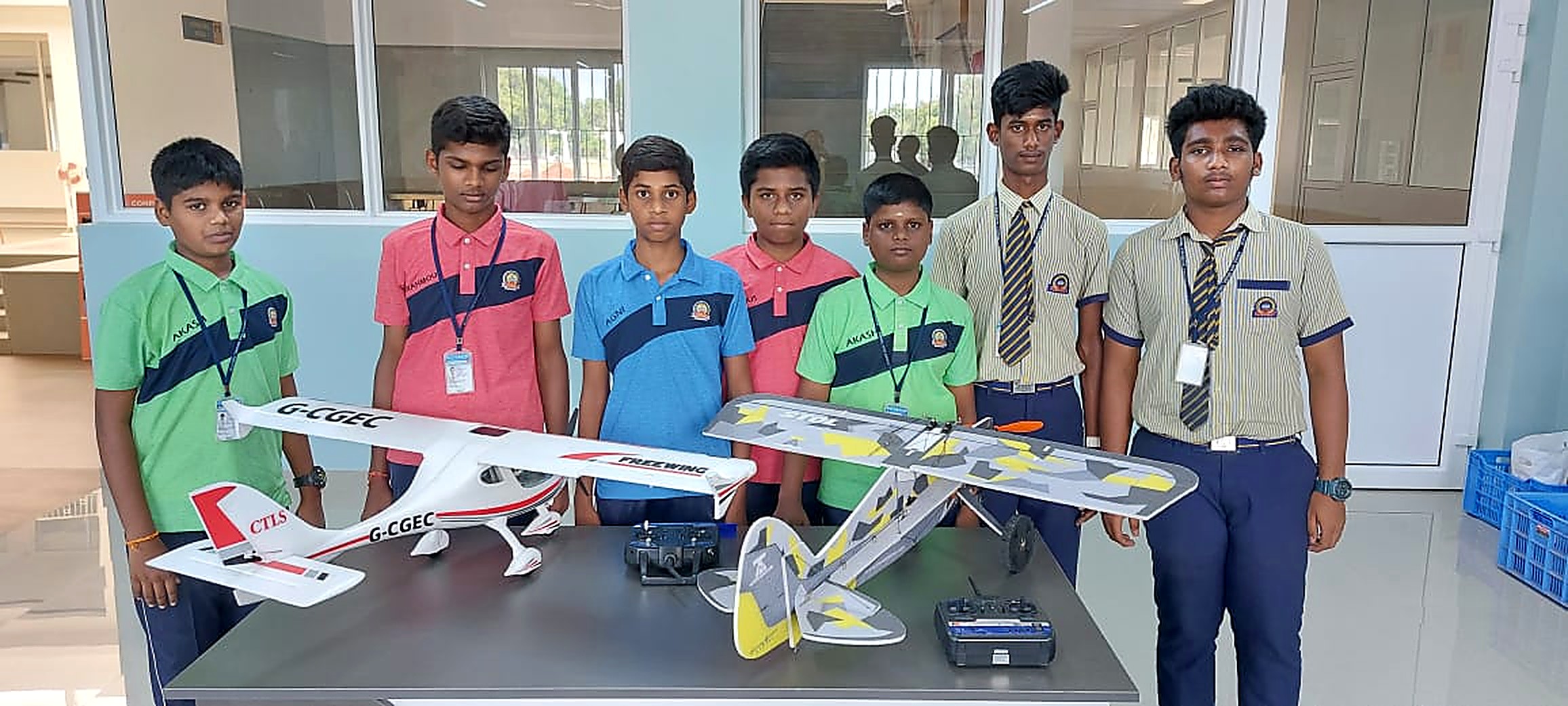 Seven school students standing behind a table with two completed radio-controlled aircraft and their transmitters