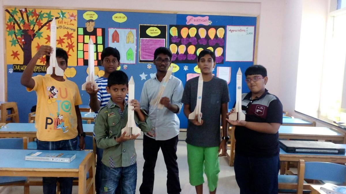 Six young students standing in a classroom and holding the white model rockets they assembled